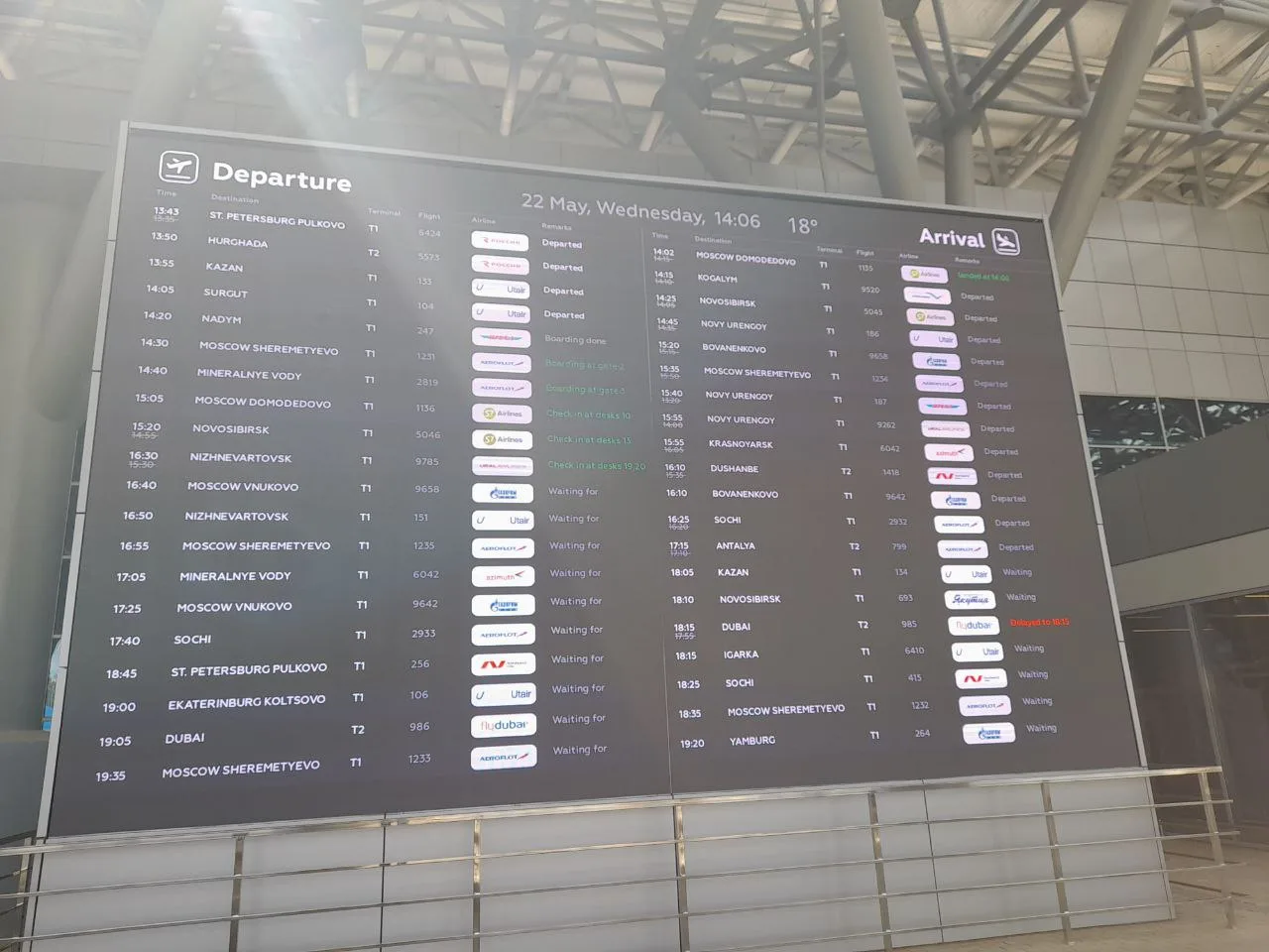 The airport's departures and arrivals LED board rendered in English by a SpinetiX player — flight times, destinations, terminals, flight numbers, airline logos and live statuses such as Departed, Boarding, Check-in and Delayed